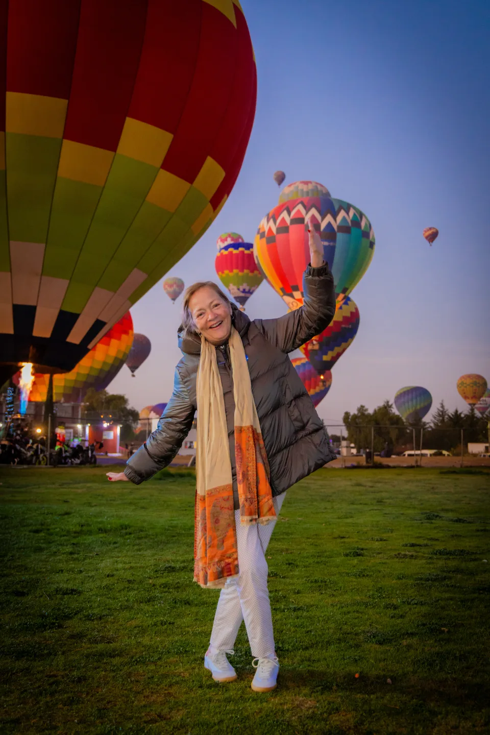 Cheerful older traveler posing with many hot air balloons at sunrise — flights for all ages